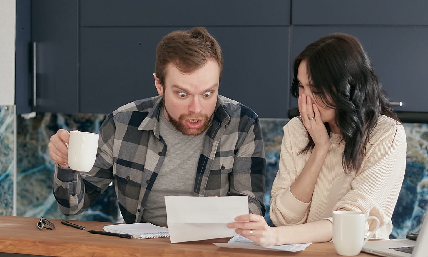 A Couple Sitting Near the Wooden Table while Looking at the Document in Shocked Emotion