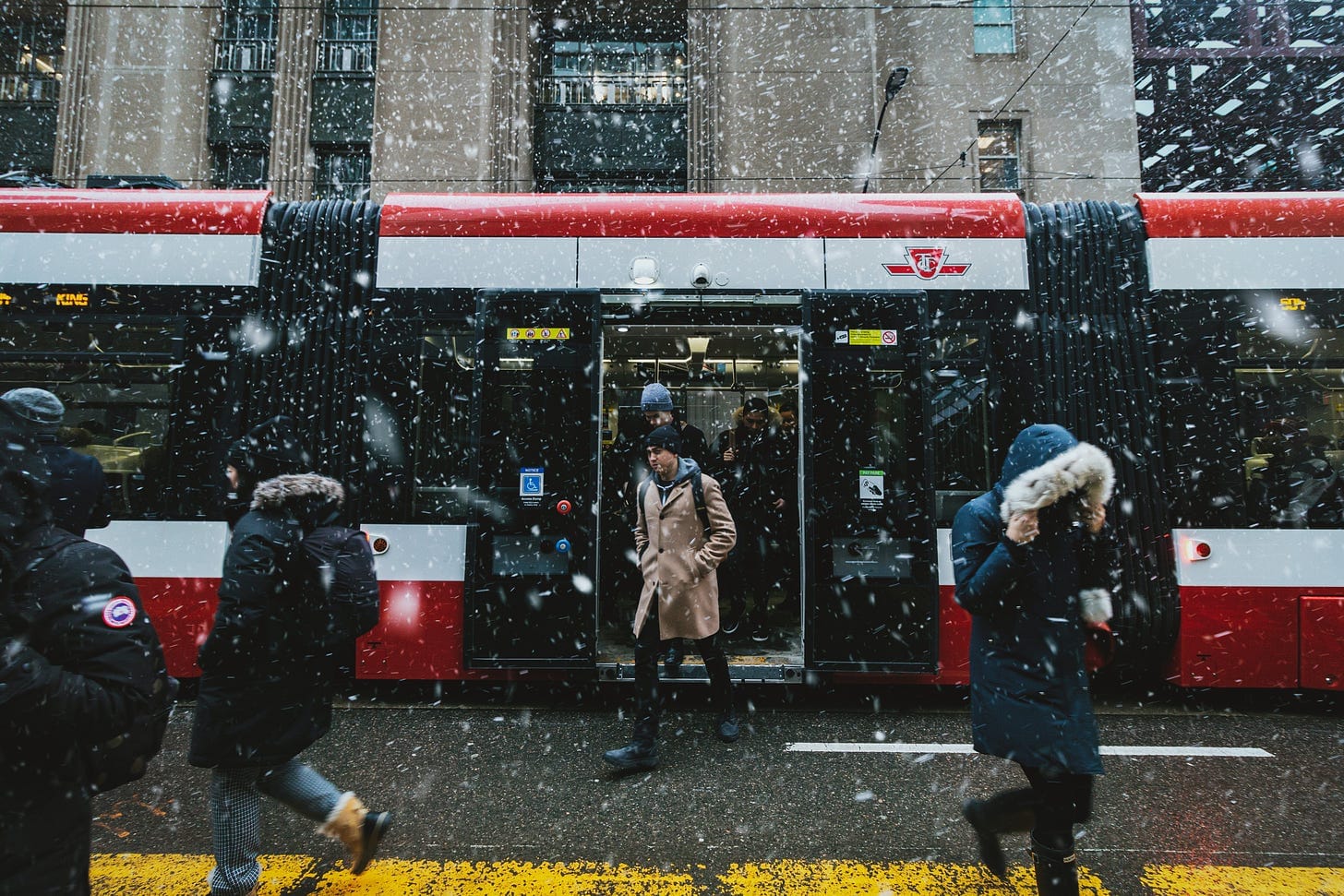 People walking in the snow outside of a streetcar in downtown Toronto