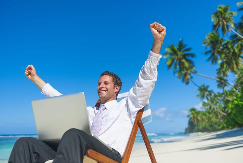 This is a photo of a man in business attire, feeling free while sitting on the beach with his laptop.